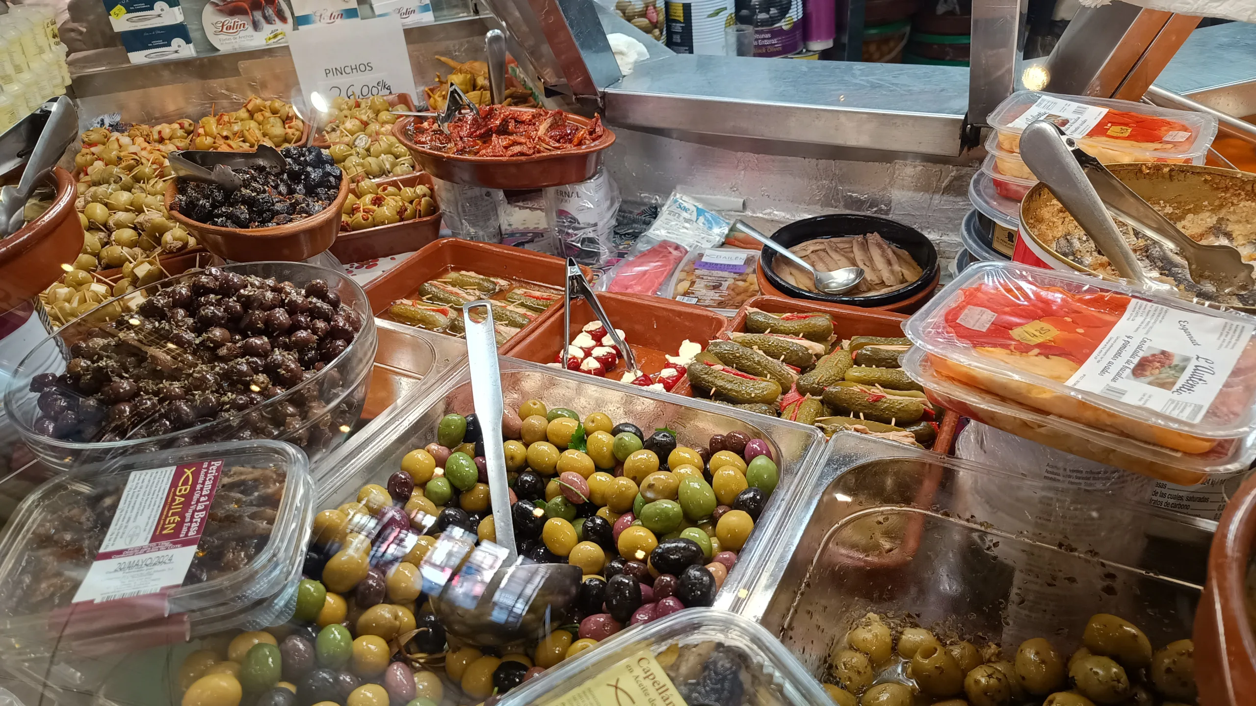 A colorful stall filled with a variety of olives and pickles at the Central Market of Alicante, featuring different types and flavors beautifully displayed in large bowls, attracting customers with their vibrant appearance and rich aroma.