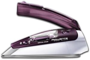 The image features the Rowenta Compact Steam Iron DA1560, showcasing its sleek, compact design with a purple exterior. The iron is positioned on a flat surface, highlighting its dual voltage feature (120V/230V), making it perfect for international travel. Next to it, there’s a small travel bag for easy portability. The mango plegable (foldable handle) is visible, emphasizing its space-saving design. The stainless steel soleplate with micro steam holes gleams, reflecting the light, while the water tank is partially filled, showing the transparent window. In the background, a neatly ironed shirt can be seen, demonstrating the iron’s efficient steam function. The Rowenta Compact Travel Steam Iron DA1560 is presented as a travel-ready and portable solution for wrinkle-free clothes on the go.